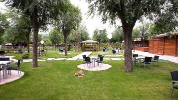 Un área de patio al aire libre con mesas y sillas, rodeada de árboles y un pabellón.