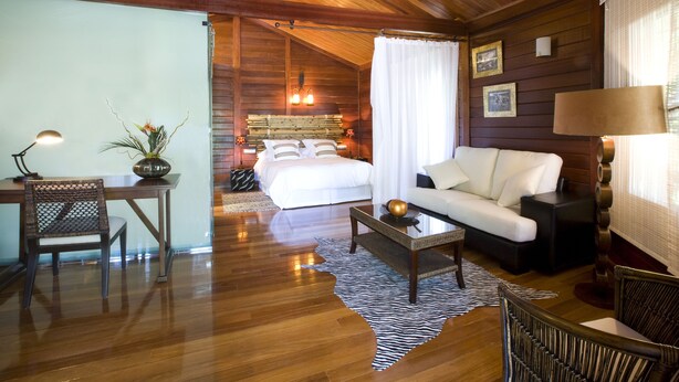 A cozy room with a wooden ceiling, a white bed, a white sofa, a dining table with chairs, and a zebra-patterned rug. - Complejo La Cigüeña (Arganda del Rey)