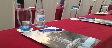 Una mesa de conferencias con mantel rojo, botellas de agua, vasos y un folleto.