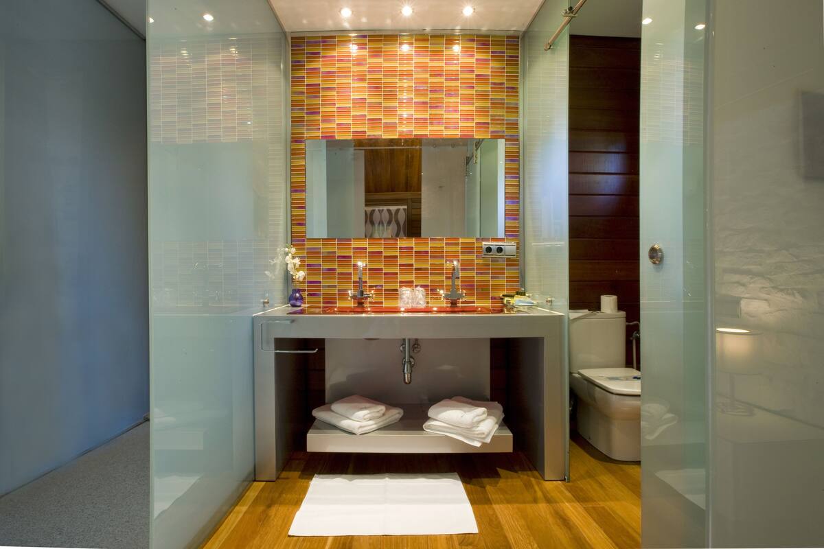 A modern bathroom with a glass-enclosed shower, a large mirror, and a colorful mosaic backsplash.