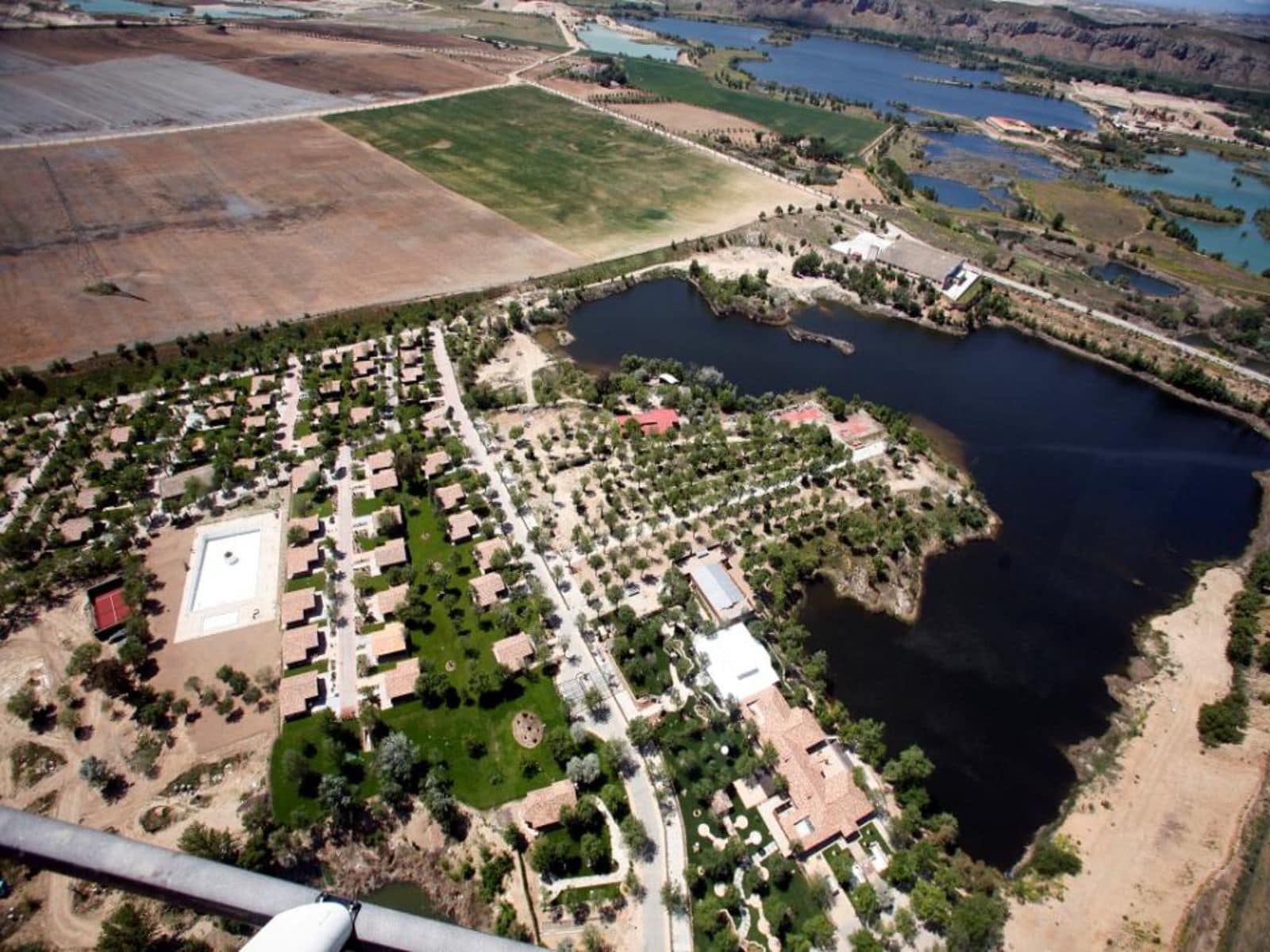 An aerial view of a residential area with a large body of water, green spaces, and a few buildings.