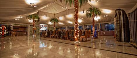 A spacious indoor venue with a high ceiling, palm trees, and a polished floor.