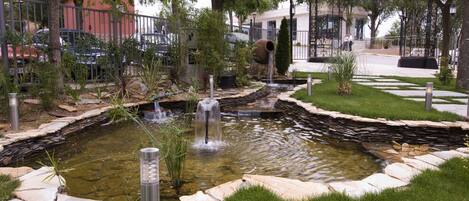 A landscaped garden with a pond, stone borders, and a metal fence.