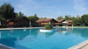 A rectangular swimming pool with clear blue water, surrounded by lounge chairs and umbrellas, and adjacent to a building with a tiled roof. - Complejo La Cigüeña (Arganda del Rey)