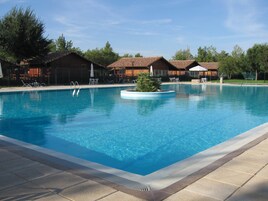 Una piscina rectangular con agua azul cristalina, rodeada de sillas de descanso y sombrillas, contigua a un edificio con techo de tejas.