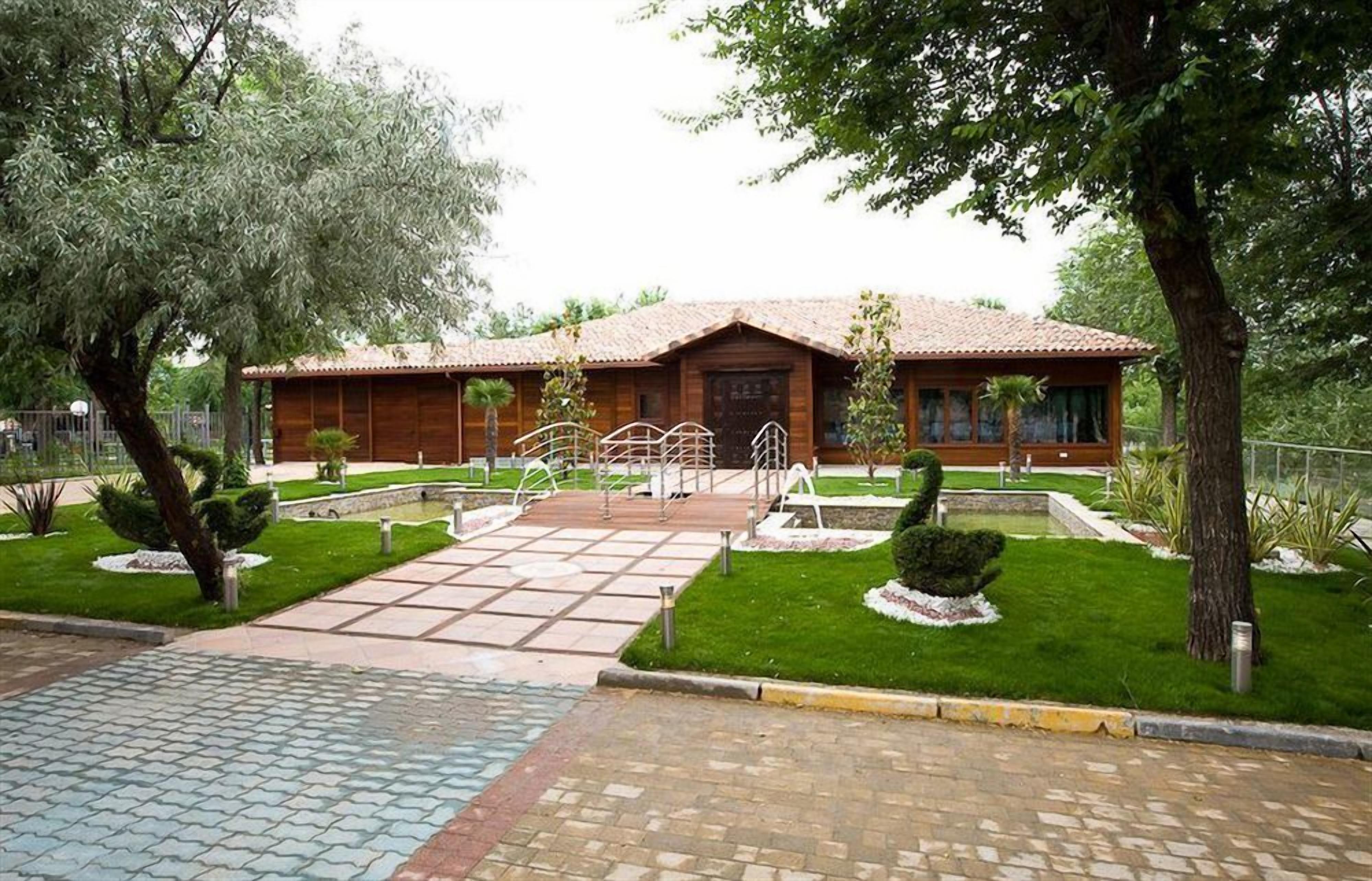 Un bâtiment en bois, surmonté d’un toit en tuiles, entouré de pelouses et d’arbres bien entretenus.