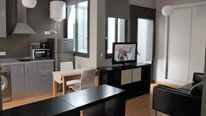 Moderni keittiö, jossa on mikroaaltouuni, liesi ja pesuallas. Keittiössä on myös ruokailutila, jossa on pöytä ja tuolit. Televisio on asennettu seinälle.