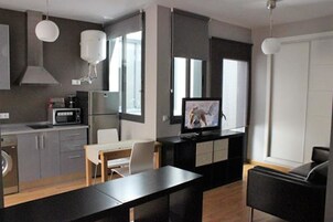 A modern kitchen with a microwave, stove, and sink. There is a dining area with a table and chairs. A television is mounted on the wall.
