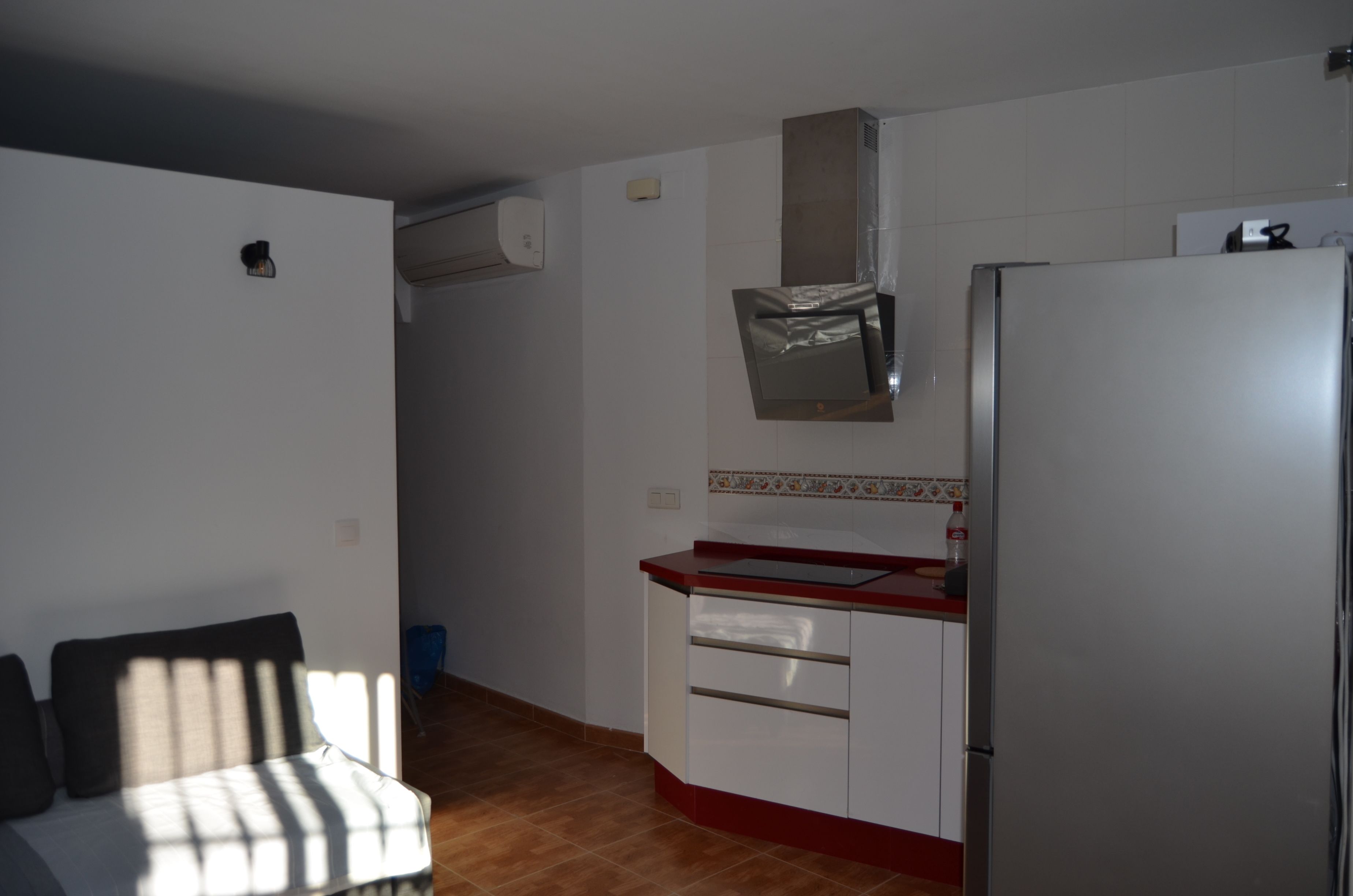 Eine kompakte Küche mit Kühlschrank, Mikrowelle und Spüle. Ein Fenster sorgt für natürliches Licht, und im angrenzenden Wohnbereich befindet sich eine Couch.