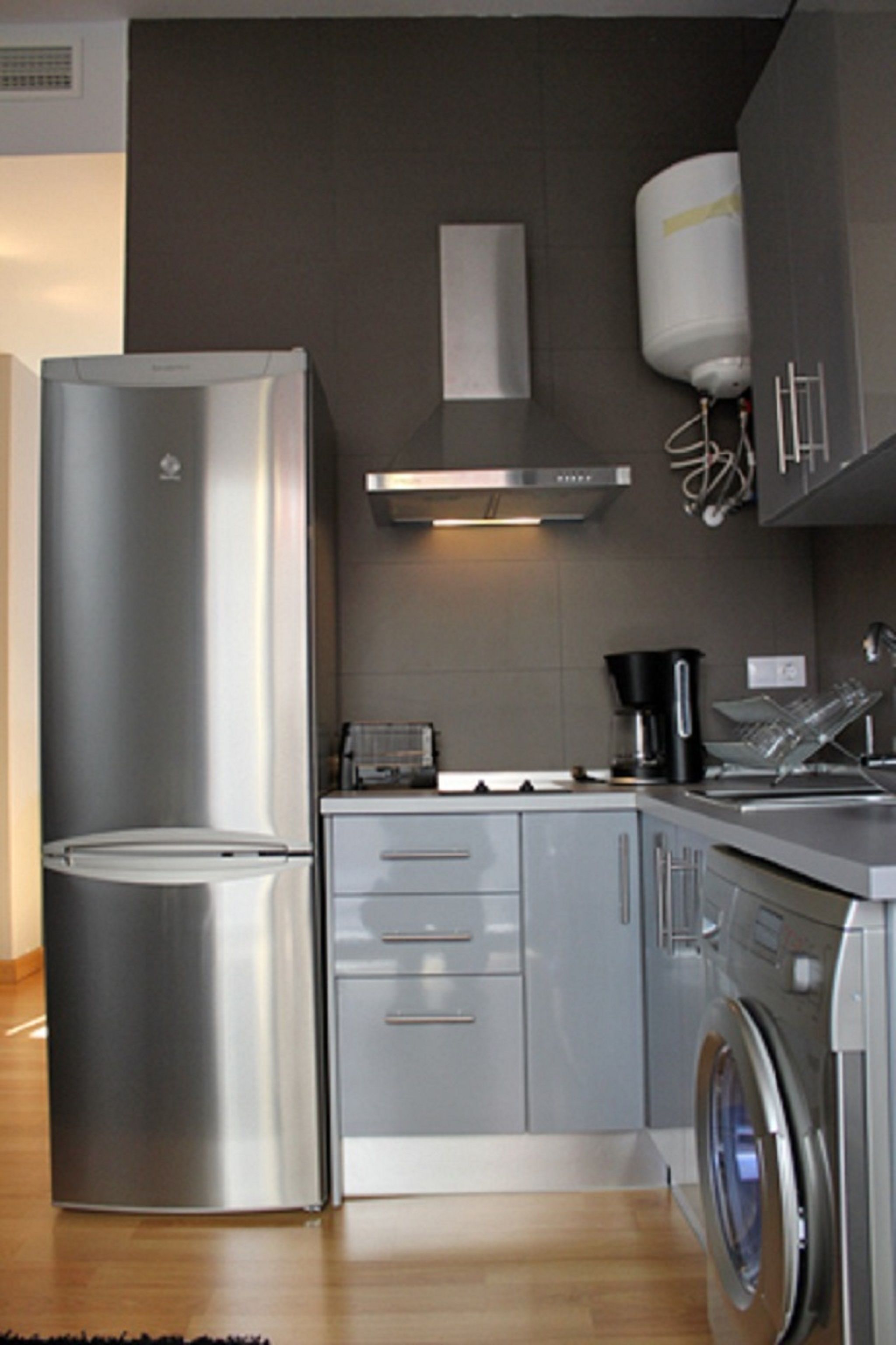 A modern kitchen with stainless steel appliances, a built-in washing machine, and grey cabinetry.