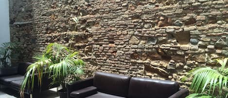 A stone wall with a leather sofa and potted plants in a courtyard.