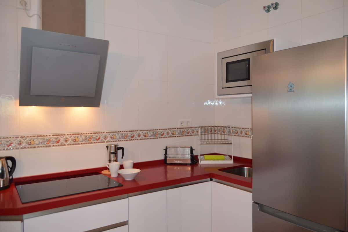 A kitchen with white cabinets, a red countertop, a stainless steel refrigerator, a microwave, and a toaster.
