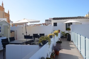 A rooftop terrace with outdoor seating, potted plants, and umbrellas.