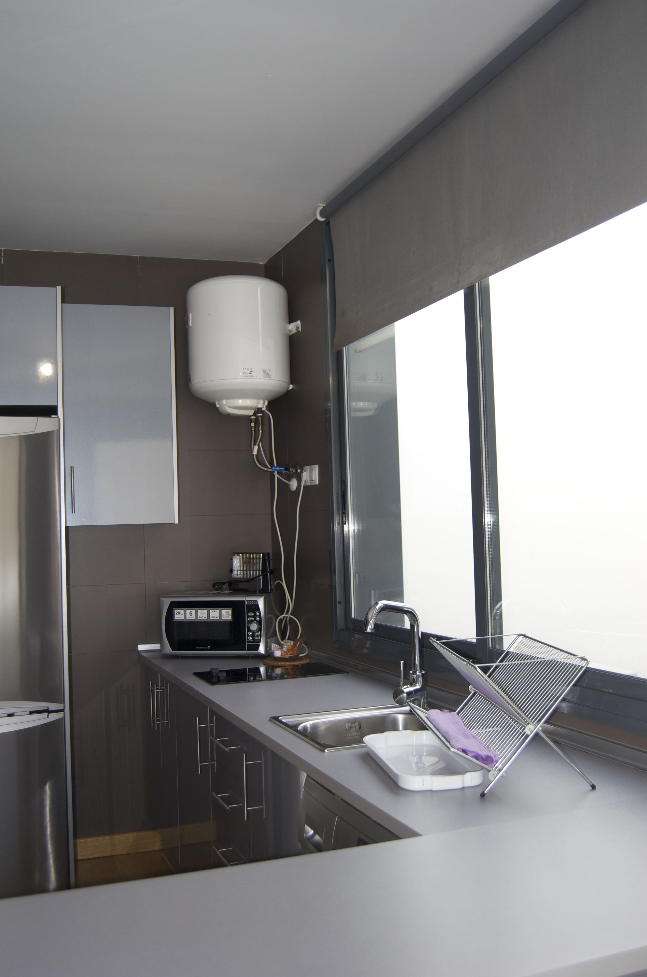 A modern kitchen with a built-in microwave, a sink with a drying rack, and a water heater mounted on the wall.