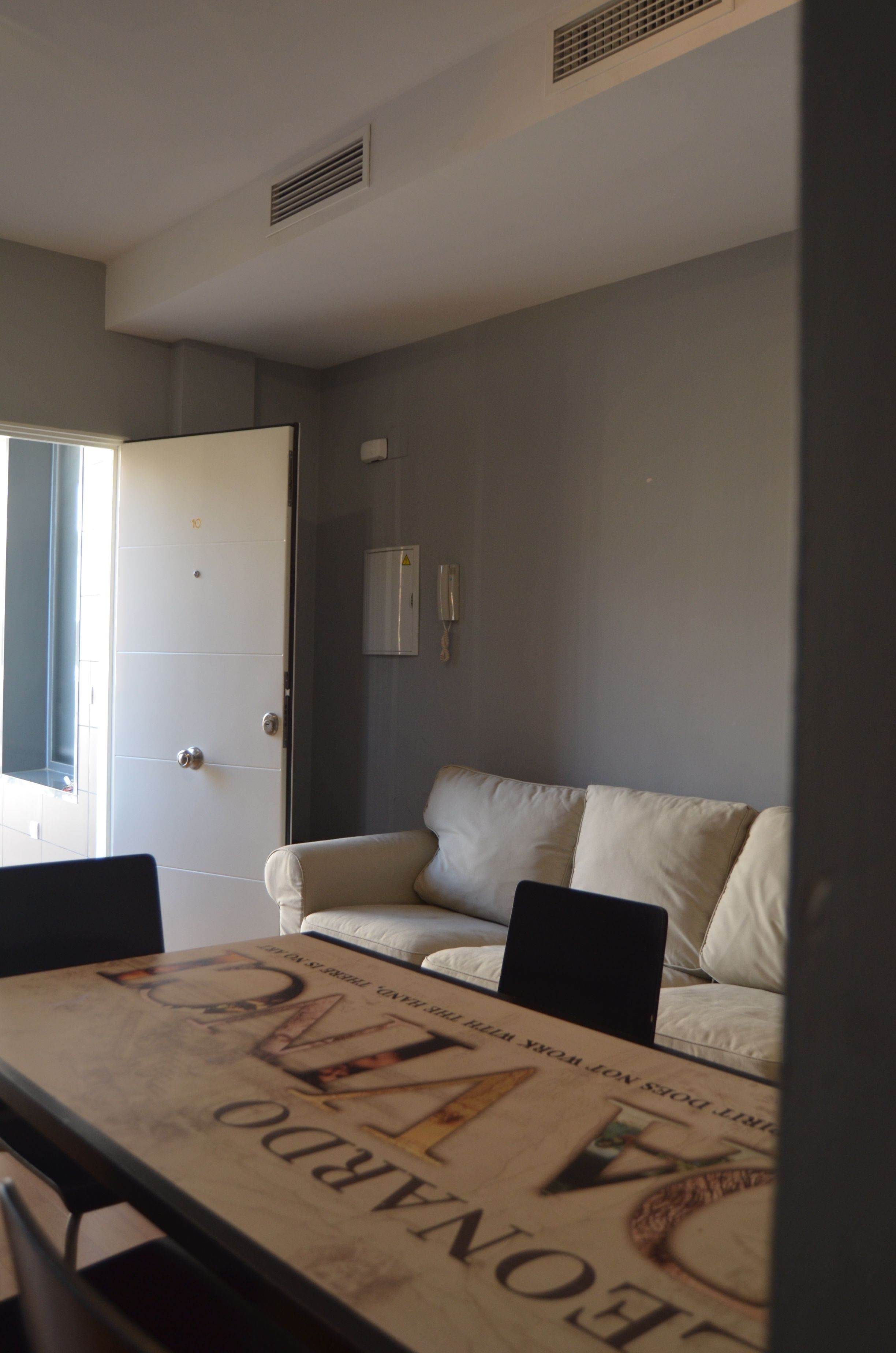 A room with a white door, a white sofa, and a table with a magazine.