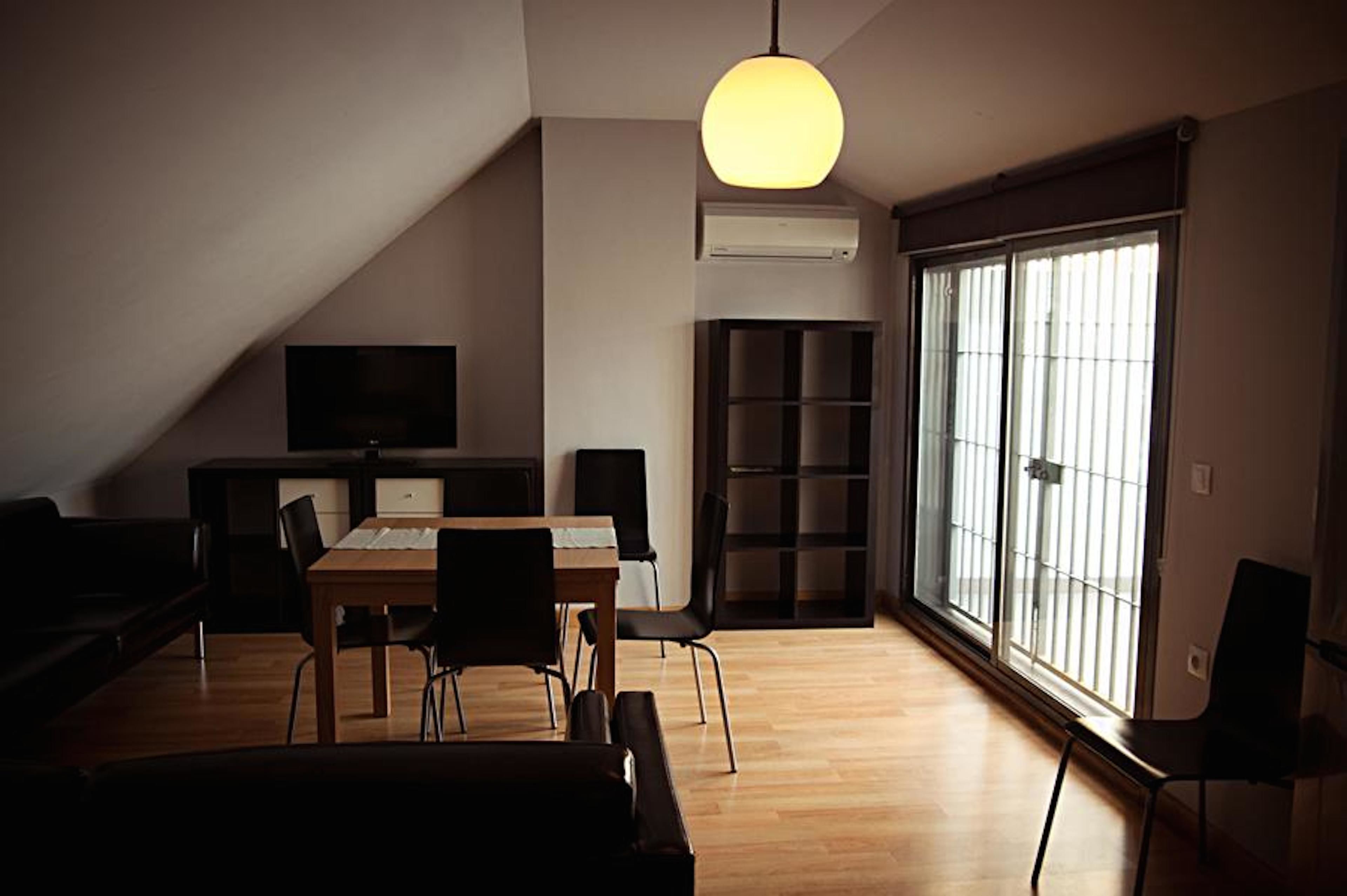 A modern living room with a dining table, chairs, a sofa, a TV, and a large window with blinds.