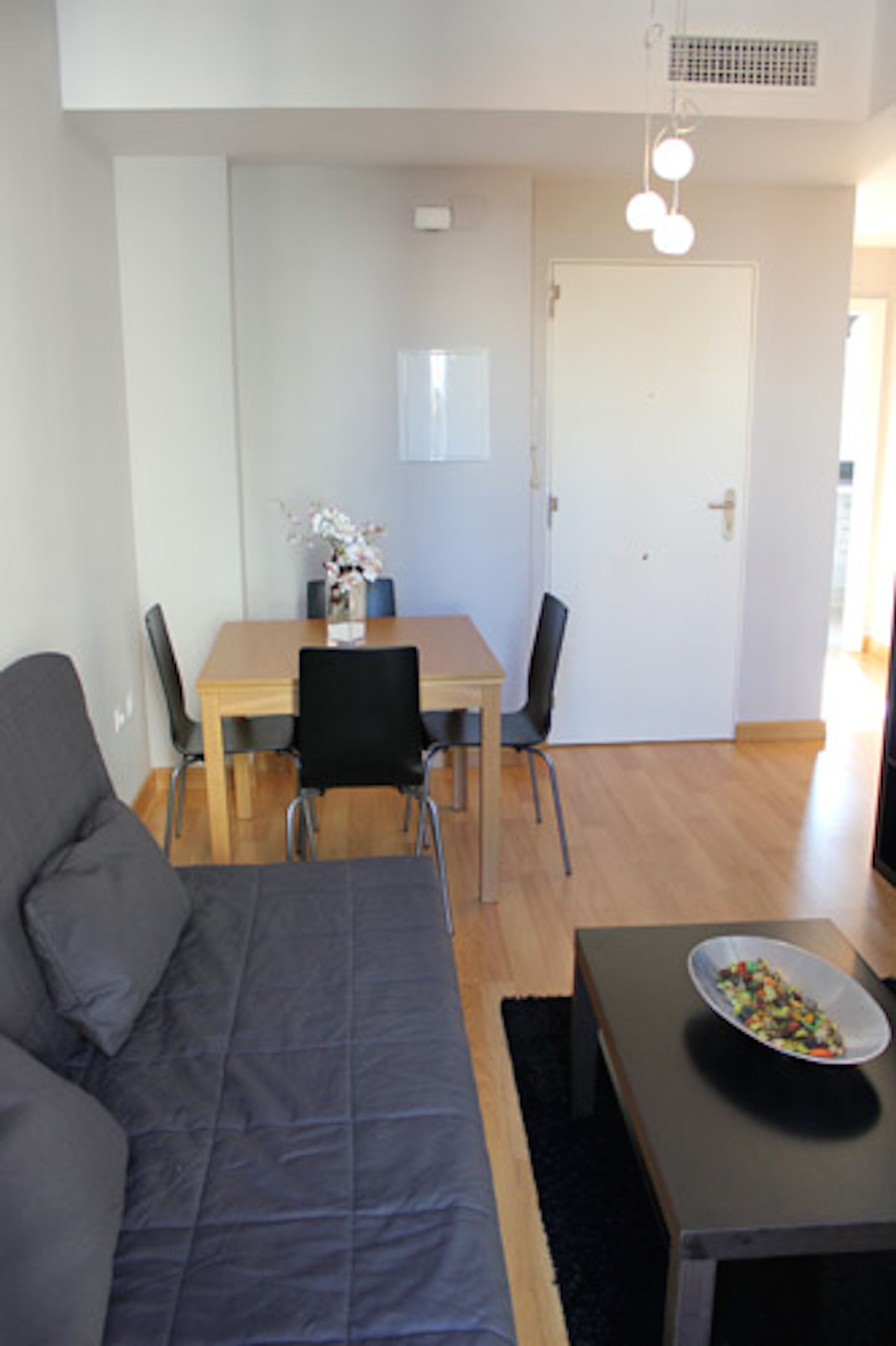A modern living room with a sofa, a dining table with chairs, and a small table with a bowl.