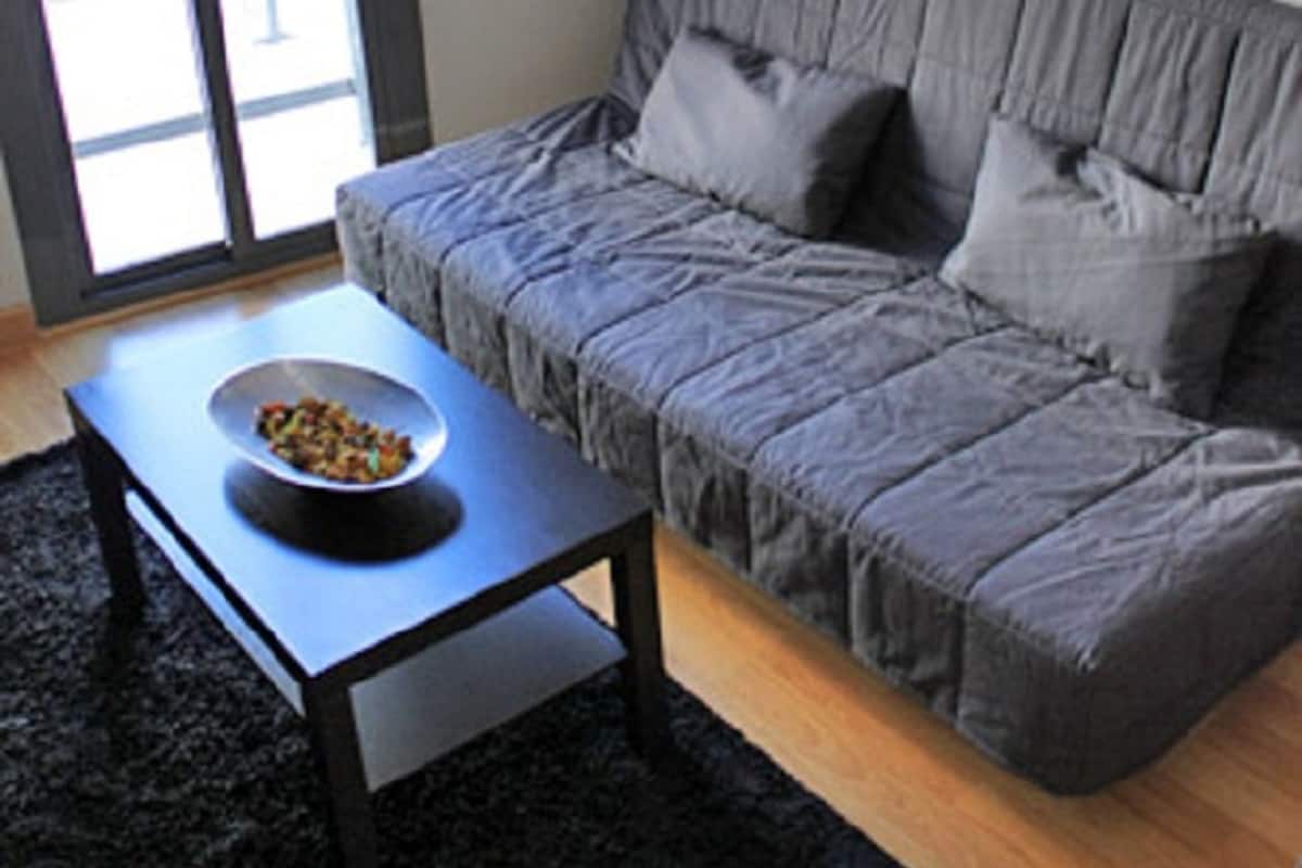 A modern living room with a grey sofa, a black rug, and a small table with a bowl.