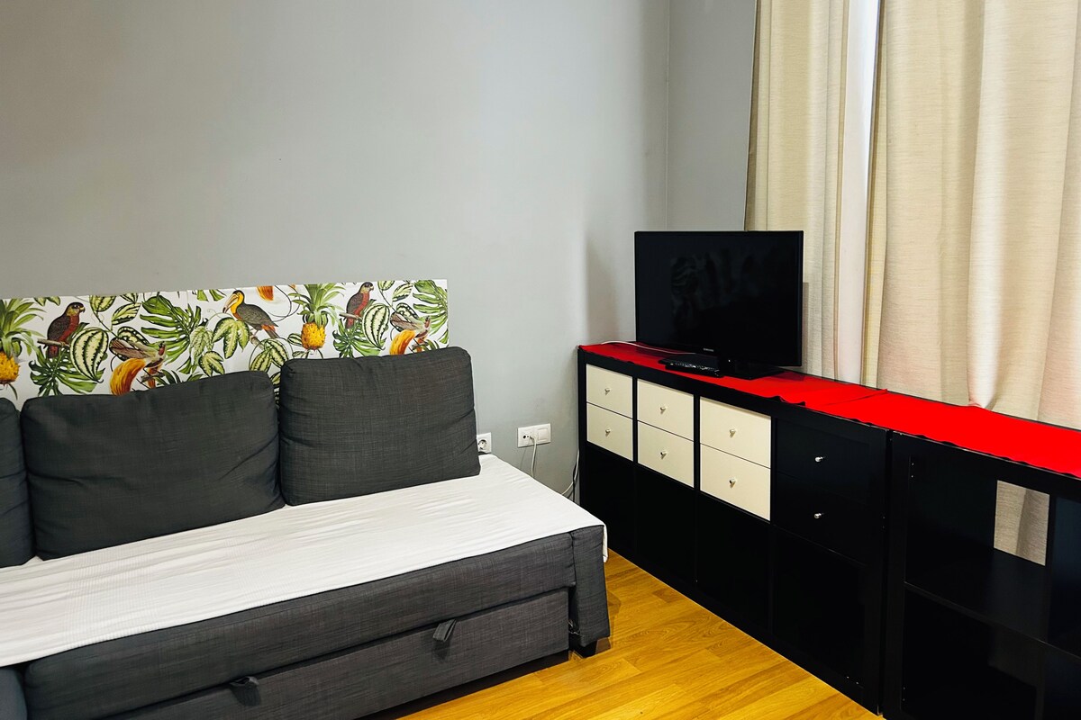 Een slaapkamer met een bed, een televisie op een zwarte kast en een muur met een tropische print.