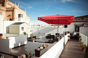 A rooftop terrace with a red umbrella, seating area, and potted plants.