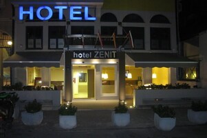 Un hotel llamado 'Hotel Zenit' con una entrada destacada, señalización iluminada y una fachada simétrica.
