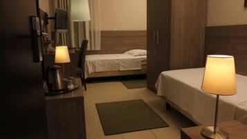 A hotel room with a bed, bedside tables, a desk with a lamp, a TV, and a coffee maker.
