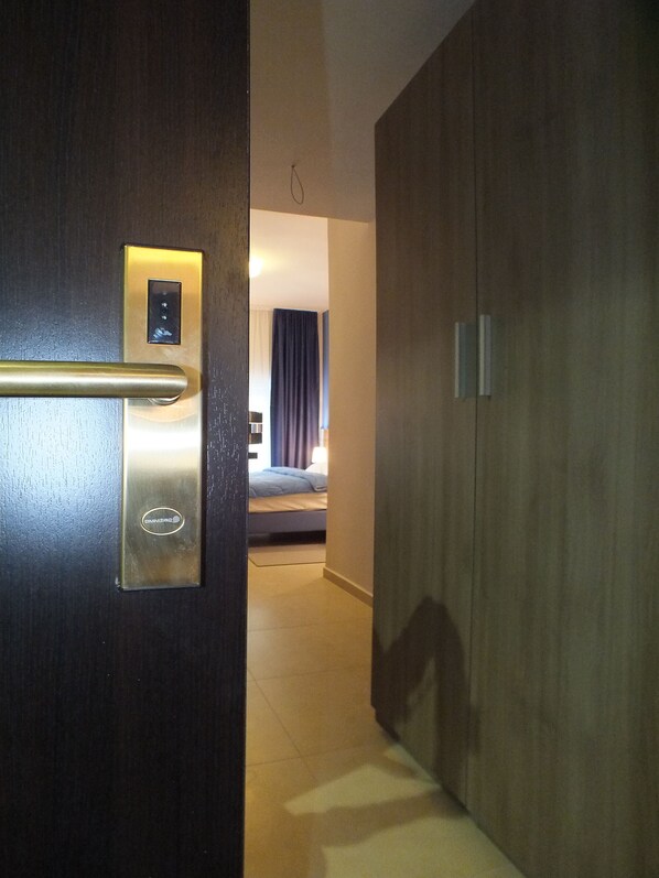 Una habitación de hotel con puerta de madera, una cama, una mesita de noche y un buró.