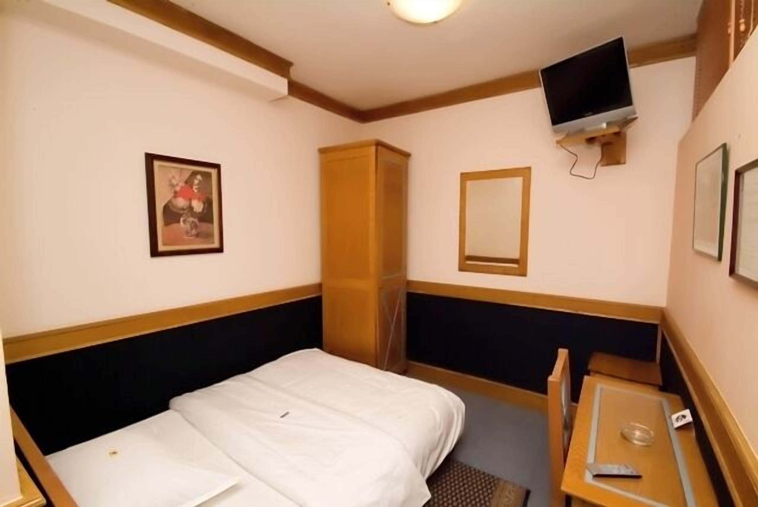Una habitación de hotel con cama, una mesita pequeña, televisor montado en la pared y armario.