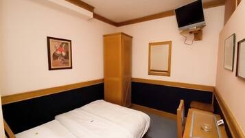Una habitación de hotel con cama, una mesita pequeña, televisor montado en la pared y armario.