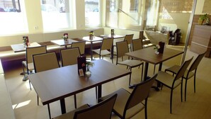 Un vaste espace dédié à la salle à manger, avec de nombreuses tables et chaises, de grandes fenêtres laissant entrer la lumière naturelle et un design épuré et moderne.