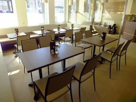 Un comedor amplio con varias mesas y sillas, ventanas grandes que dejan entrar luz natural y un diseño moderno y limpio.