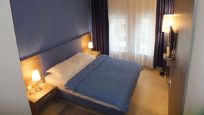 Une chambre d’hôtel avec un lit, deux tables de chevet avec des lampes, une télévision et une fenêtre avec des rideaux.