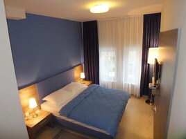 Una habitación de hotel con cama, dos mesitas de noche con lámparas, un televisor y una ventana con cortinas.