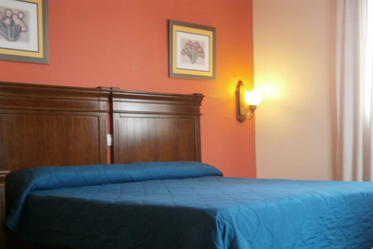 Un dormitorio con cabecera de madera, colcha azul y dos cuadros con motivos florales en la pared.