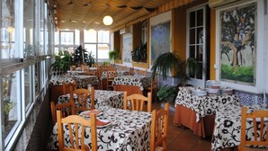 Een restaurant met meerdere tafels, bedekt met tafelkleden met een patroon, houten stoelen en potplanten.