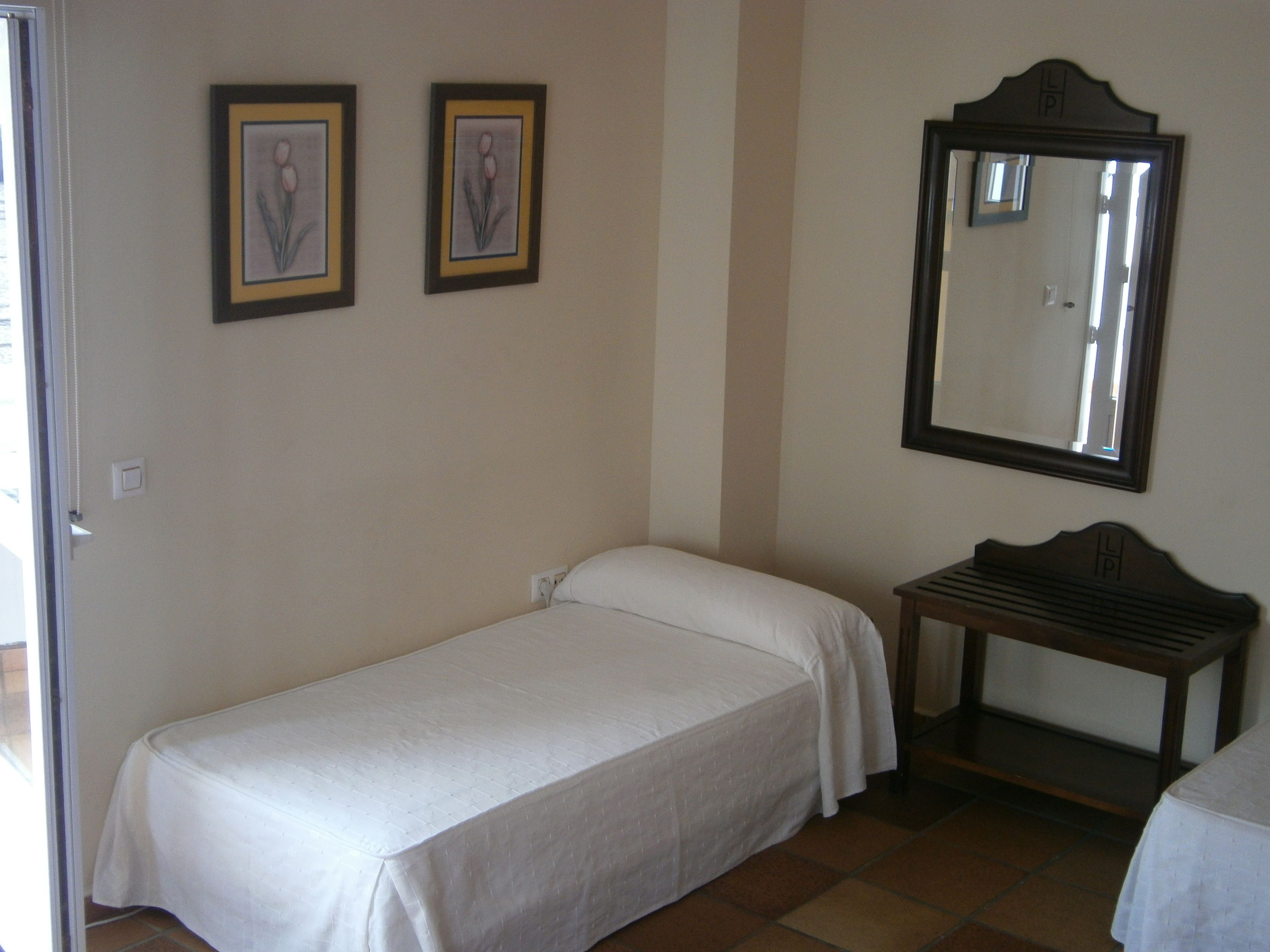 Ein kleines, ordentlich eingerichtetes Schlafzimmer mit einem Einzelbett, einem Nachttisch und zwei gerahmten Bildern an der Wand.
