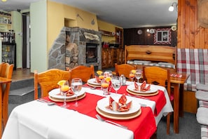 A dining area with a stone fireplace, wooden furniture, and a red tablecloth. - Pension Goralturist (Zdiar)