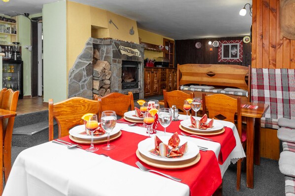 Un comedor con chimenea de piedra, muebles de madera y mantel rojo.