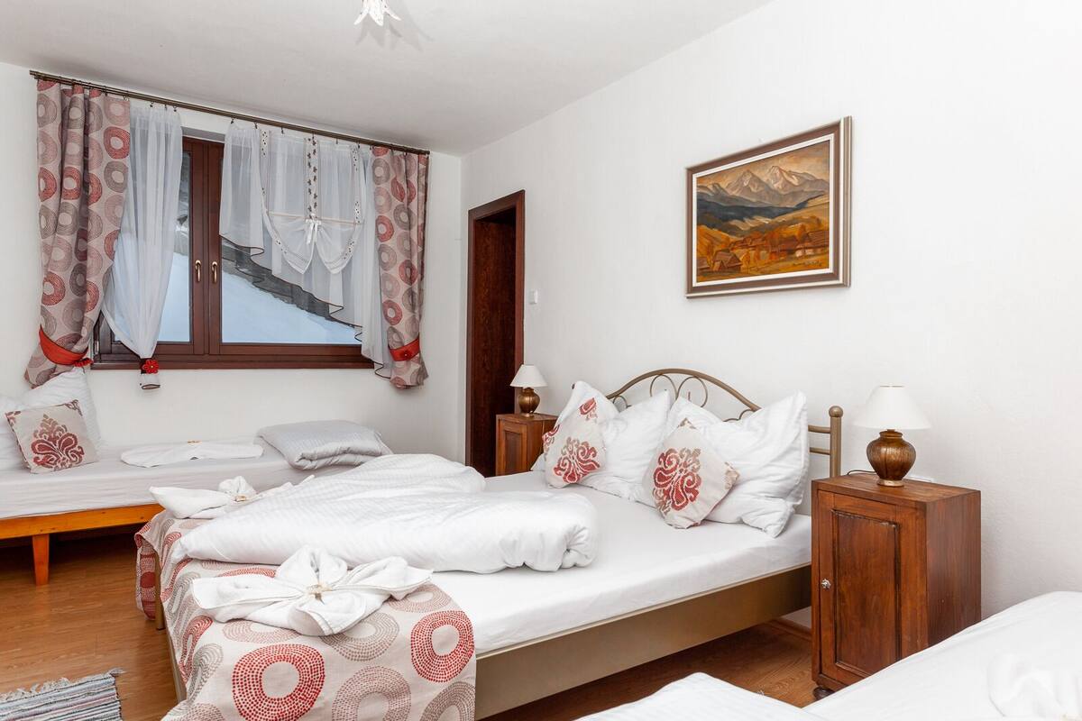 A hotel room with a bed, a bedside table with lamps, a painting on the wall, and a window with curtains.