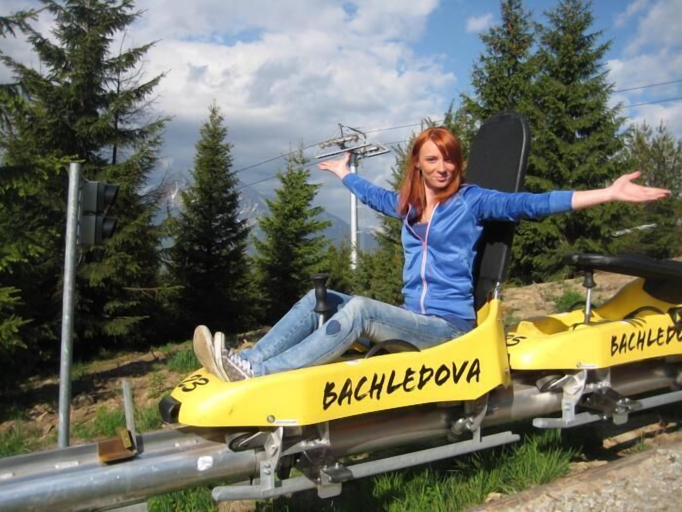 En person sidder på en gul stol med teksten "BACHLEDOVA", på en sti med træer i baggrunden.