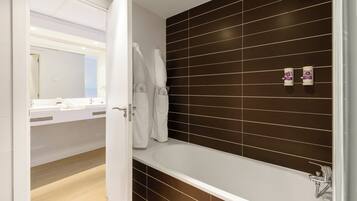 Une salle de bain moderne avec une baignoire, des carreaux de couleur marron foncé, un lavabo blanc et un miroir.