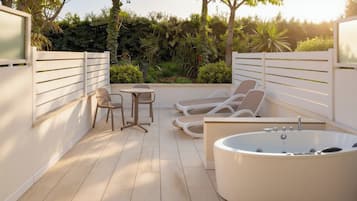 Un espace de détente extérieur moderne, doté d’une grande baignoire, de chaises longues et d’une petite table.