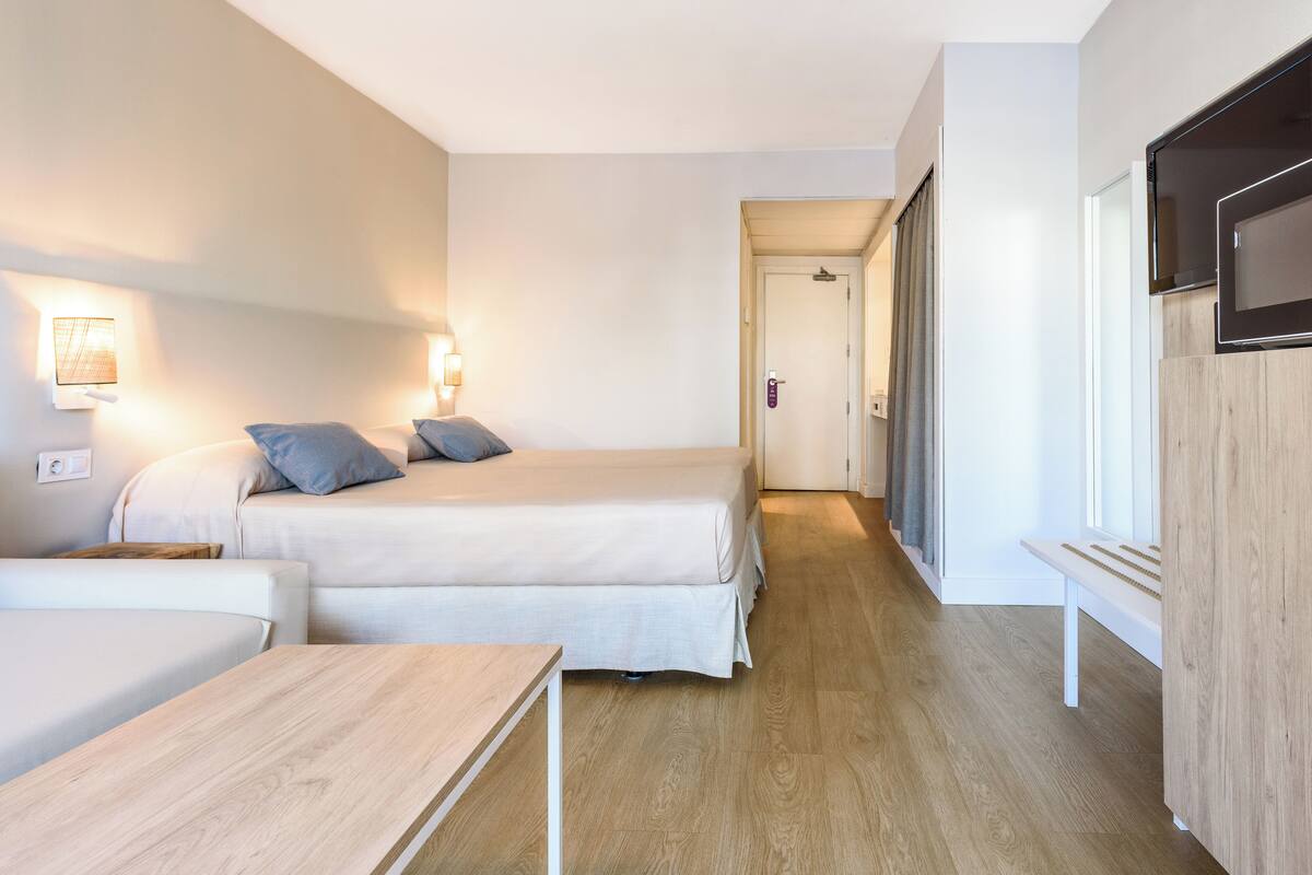 A hotel room with two beds, a wooden table, a TV, and a bench.