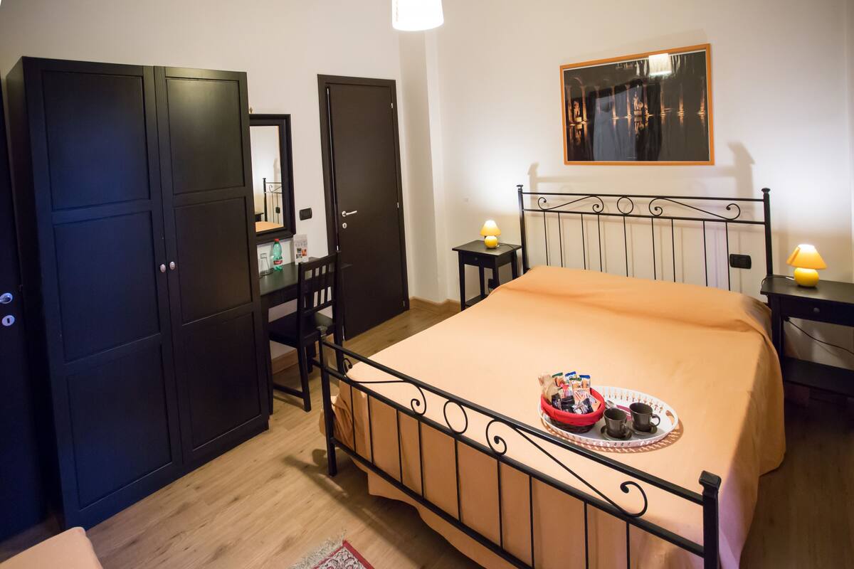 A bedroom with a bed, wardrobe, bedside tables, and a mirror.