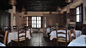 A dining area with wooden tables and chairs, a tiled floor, and hanging wicker lamps. - Hotel San Roque (La Taha)