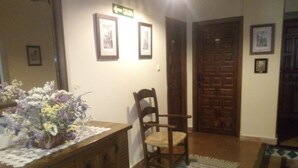 A hallway with a wooden chair, a wooden dresser with a floral arrangement, and a door with a sign. - Hotel San Roque (La Taha)