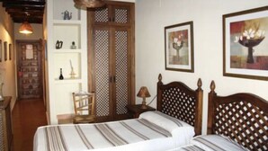 A bedroom with a bed, wooden headboard, a nightstand, a lamp, a chair, a wardrobe, and a shelf with decorative items. - Hotel San Roque (La Taha)
