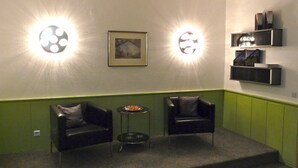 A room with two leather armchairs, a small table with a plate of food, and wall-mounted shelves with books and decorative items. - Hotel Sechzehn (Leverkusen)