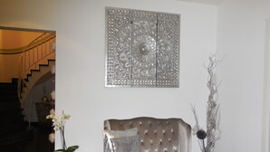 A modern living room with a tufted sofa, a decorative wall piece, a small side table with a plant, and a staircase in the background. - Hotel Sechzehn (Leverkusen)