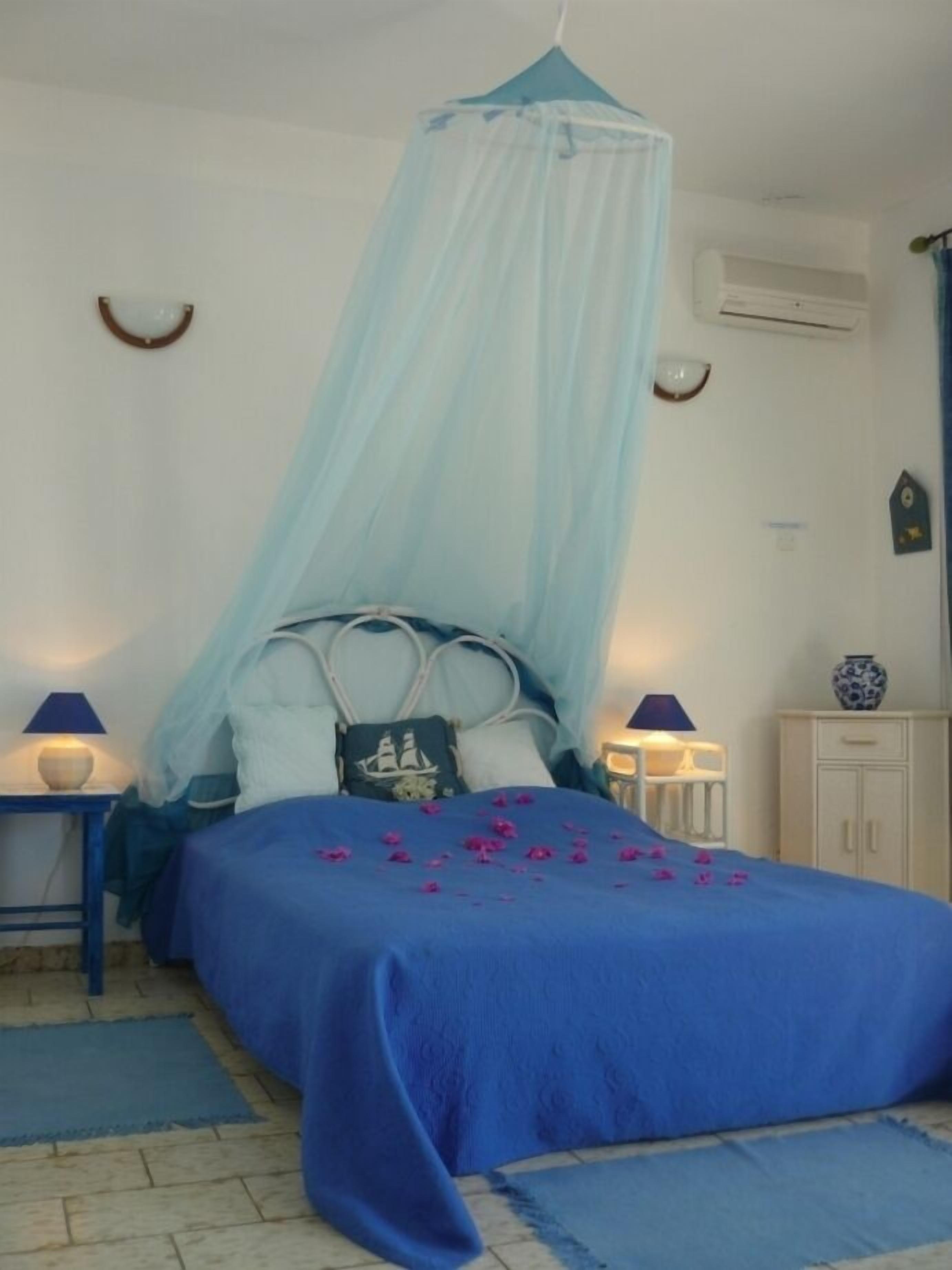 A bedroom with a canopy bed, a bedside table with a lamp, a small cabinet, and a decorative vase.